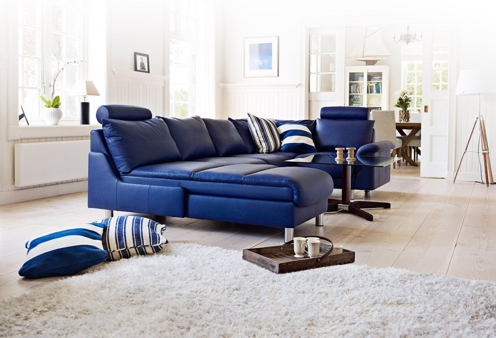 Синий диван из кожзама является акцентным элементом в интерьере белой гостиной