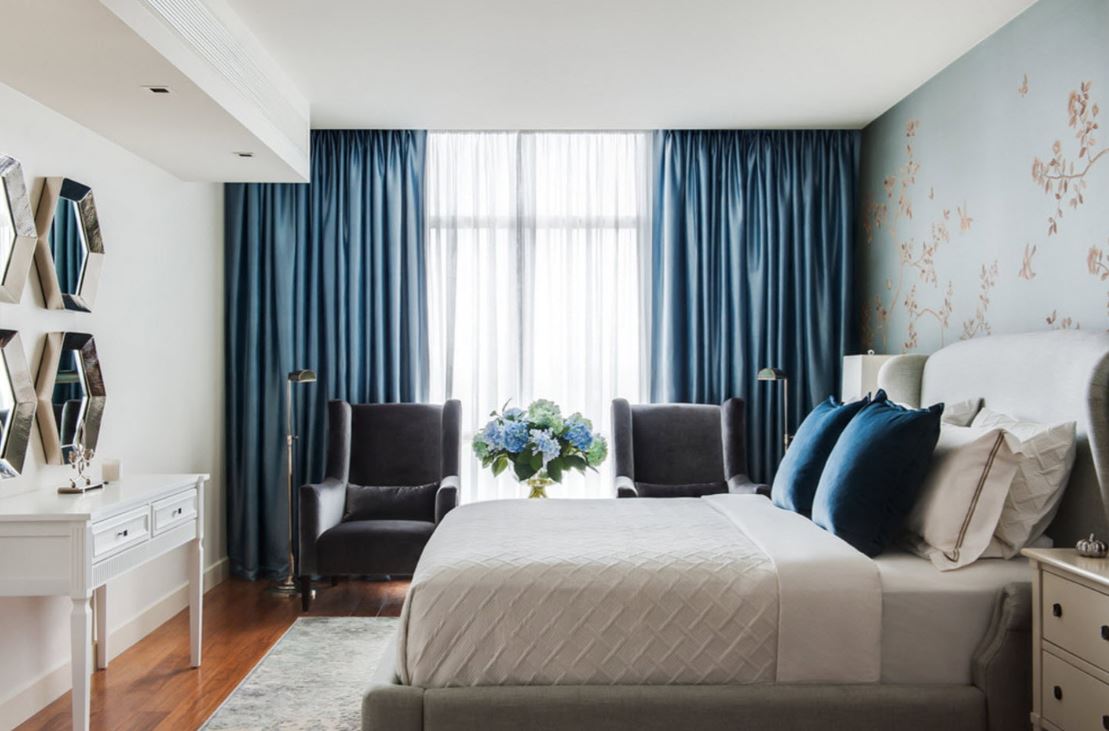 Синие шторы и полушки создают необходимый акцент в бежево-молочном интерьере современной спальни