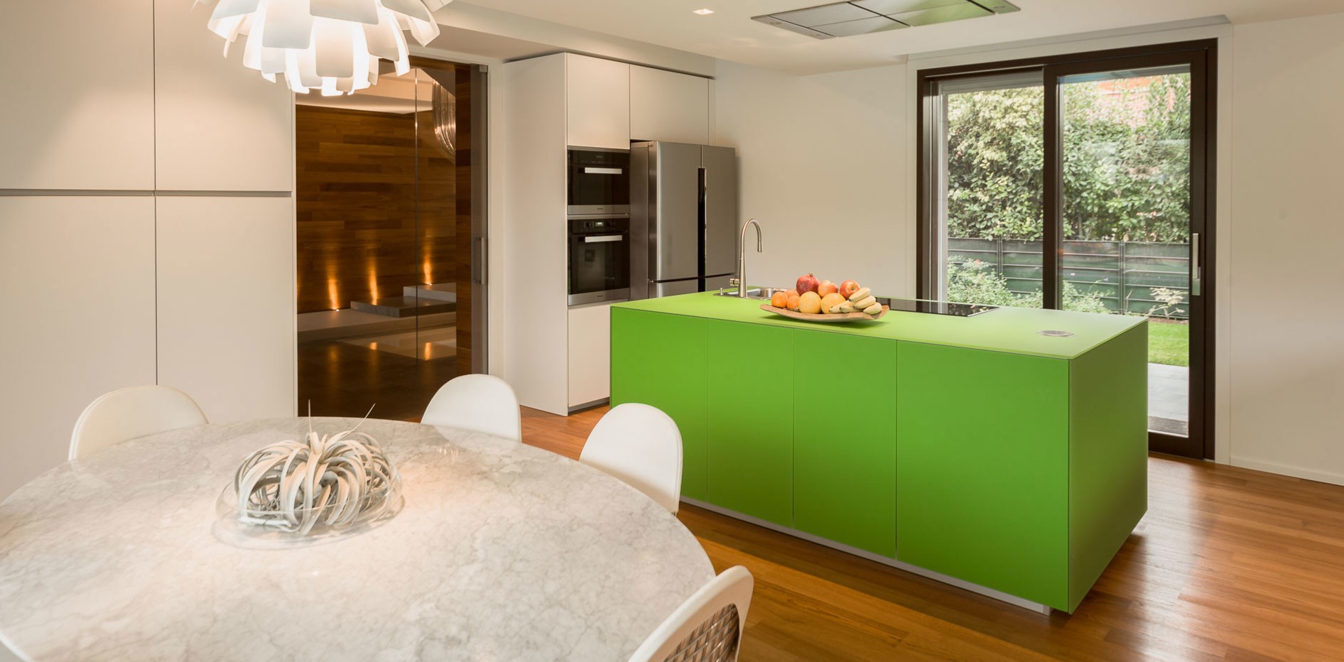 Зеленый кухонный остров является акцентным элементом в интерьере белой кухни