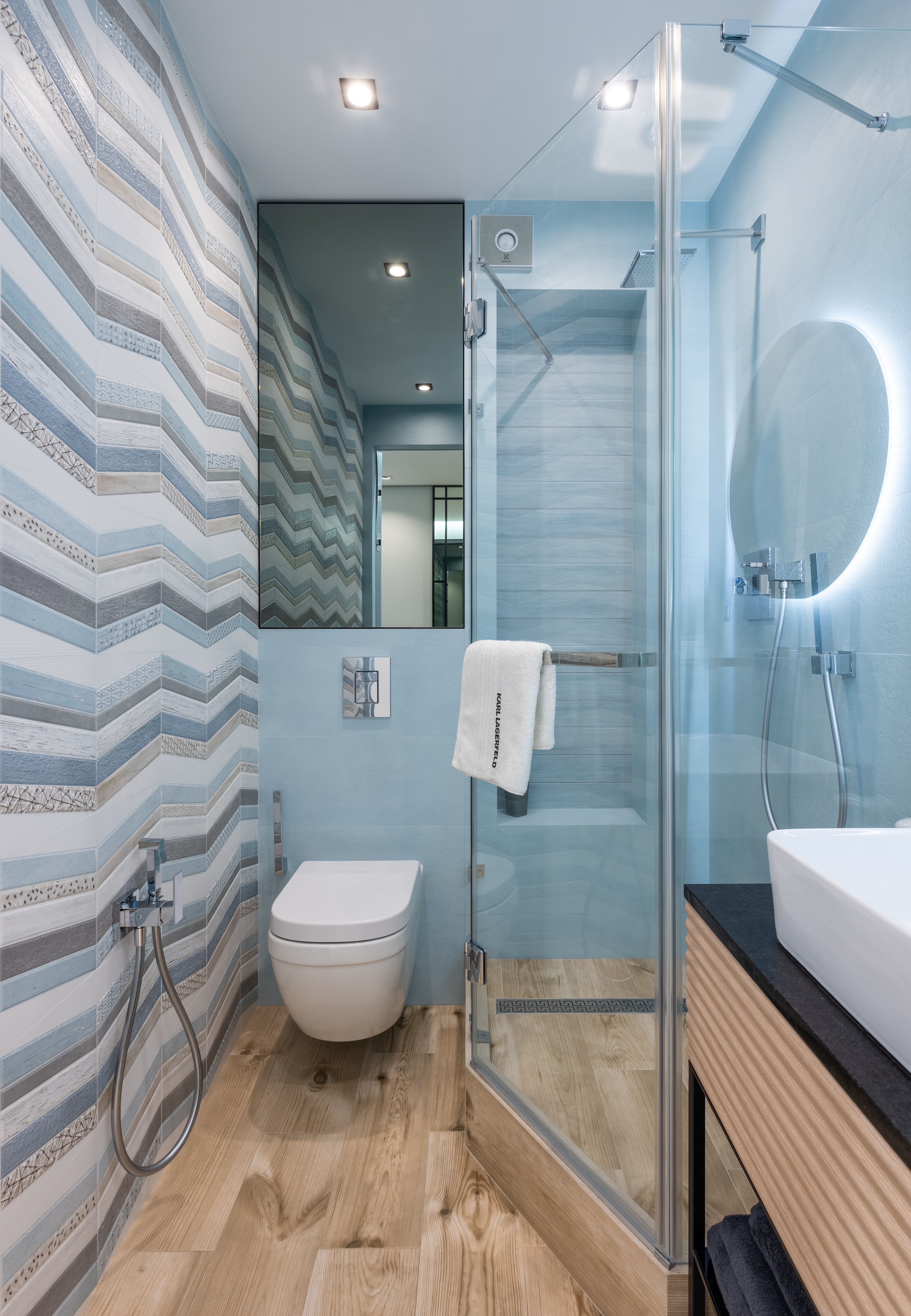 Глянцевый потолок в узкой ванной комнате визуально увеличивает пространство, свою лепту вносит и прямоугольное вертикальное зеркало.