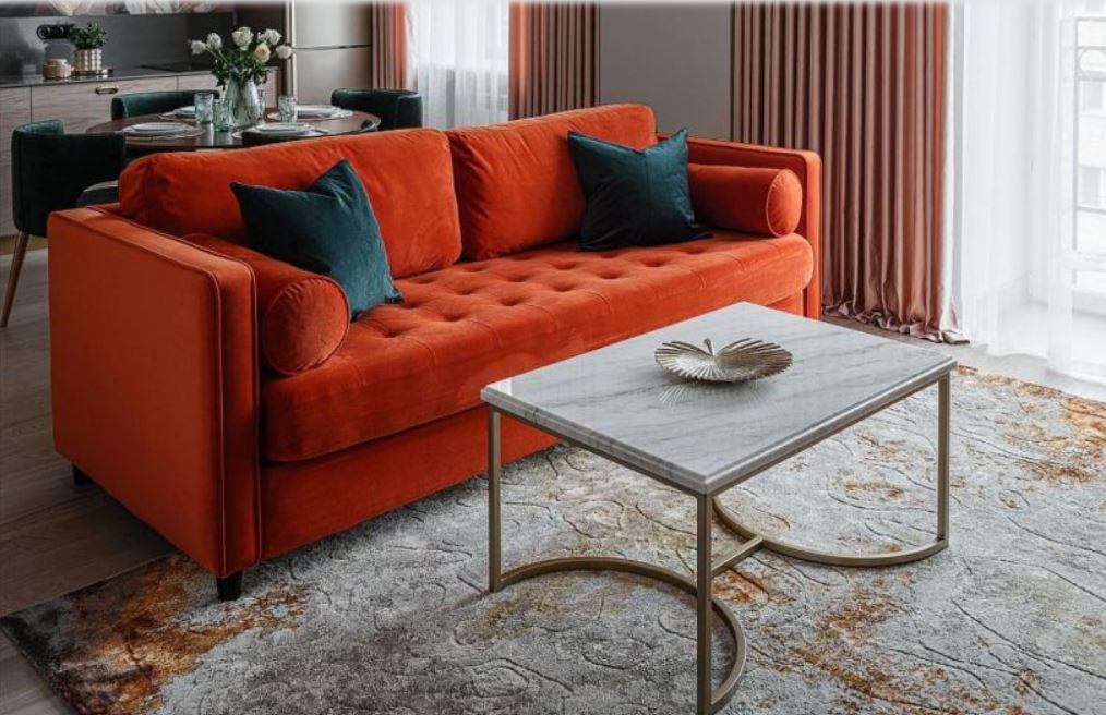 Яркий оранжевый диван разделяет гостиную и кухню на зоны