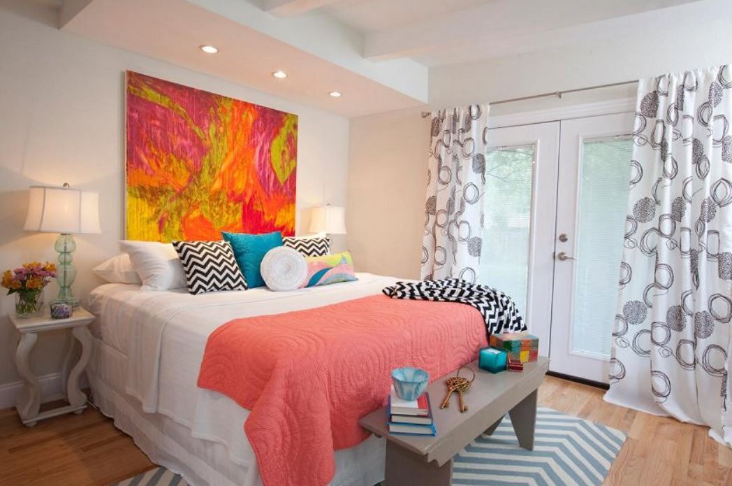 Абстрактная картина в изголовье, покрывало цвета лосося и несколько контрастных подушек создают позитивную атмосферу в спальне