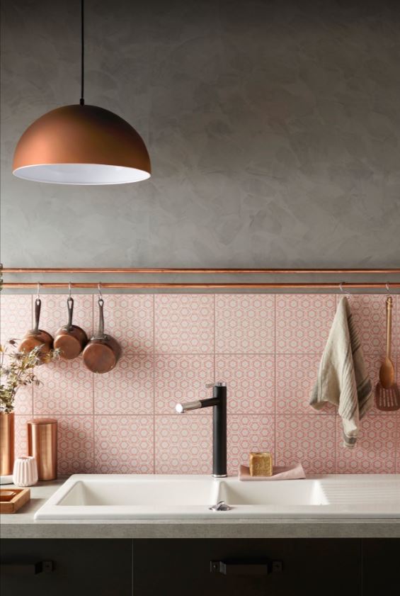 Розовый «фартук» интересно смотрится на фоне графитово-серой отделки стен и мебели в сочетании с уютным блеском меди на кухне